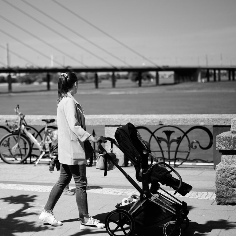 Eine Mama schiebt ihren Kinderwagen entlang des Rheins durch Düsseldorf